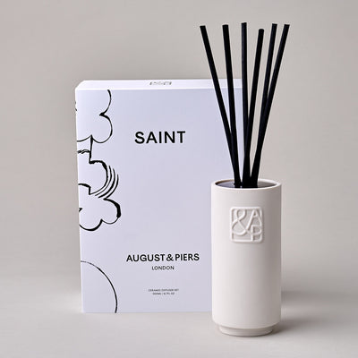 AUGUST&PIERS white ceramic diffuser with embossed 'A&P' logos on the front, displayed alongside their packaging box featuring an illustration by Petra Börner, set against a neutral background.