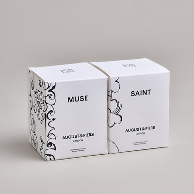 The Inspiring Duo Gift Set by AUGUST&PIERS London. Two classic ceramic candles are packaged in a limited-edition dark gold box. This set features the Muse and Saint candles.