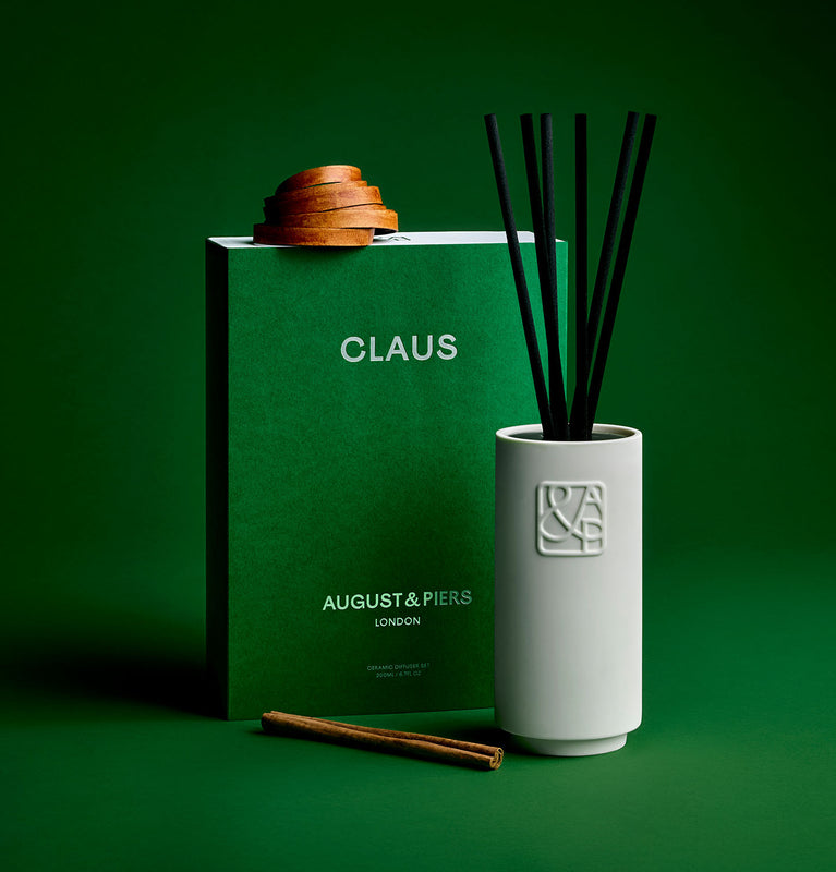 A white ceramic diffuser with black rattan reeds, featuring a logo on the front, designed to complement any space.