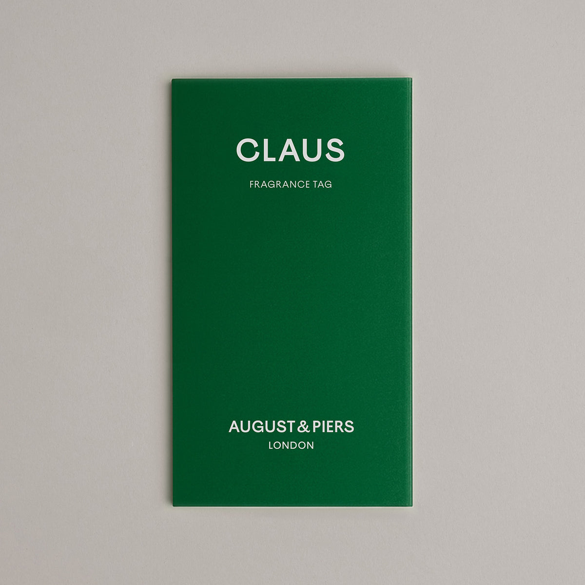 Green fragrance tag with 'Claus' and 'August & Piers London' text on a gray background