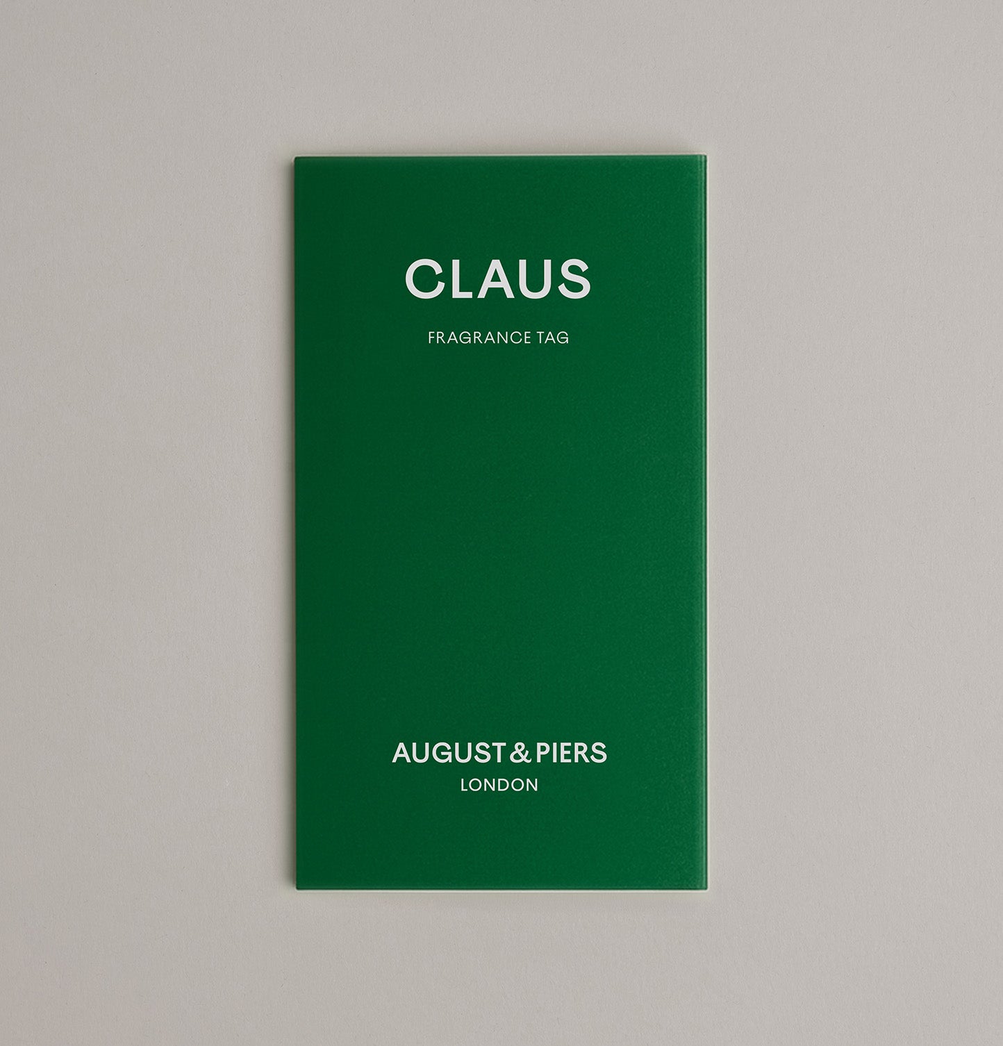 Green fragrance tag with 'Claus' and 'August & Piers London' text on a gray background