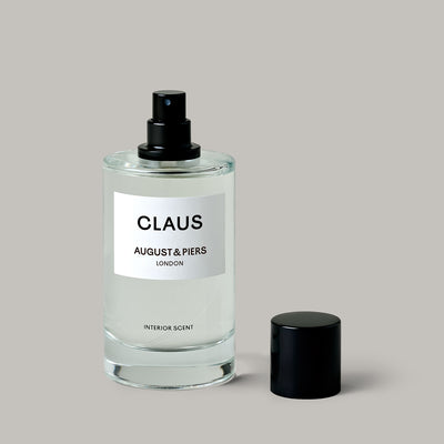 Clear glass bottle with black cap labeled 'Claus' by August & Piers on a gray background