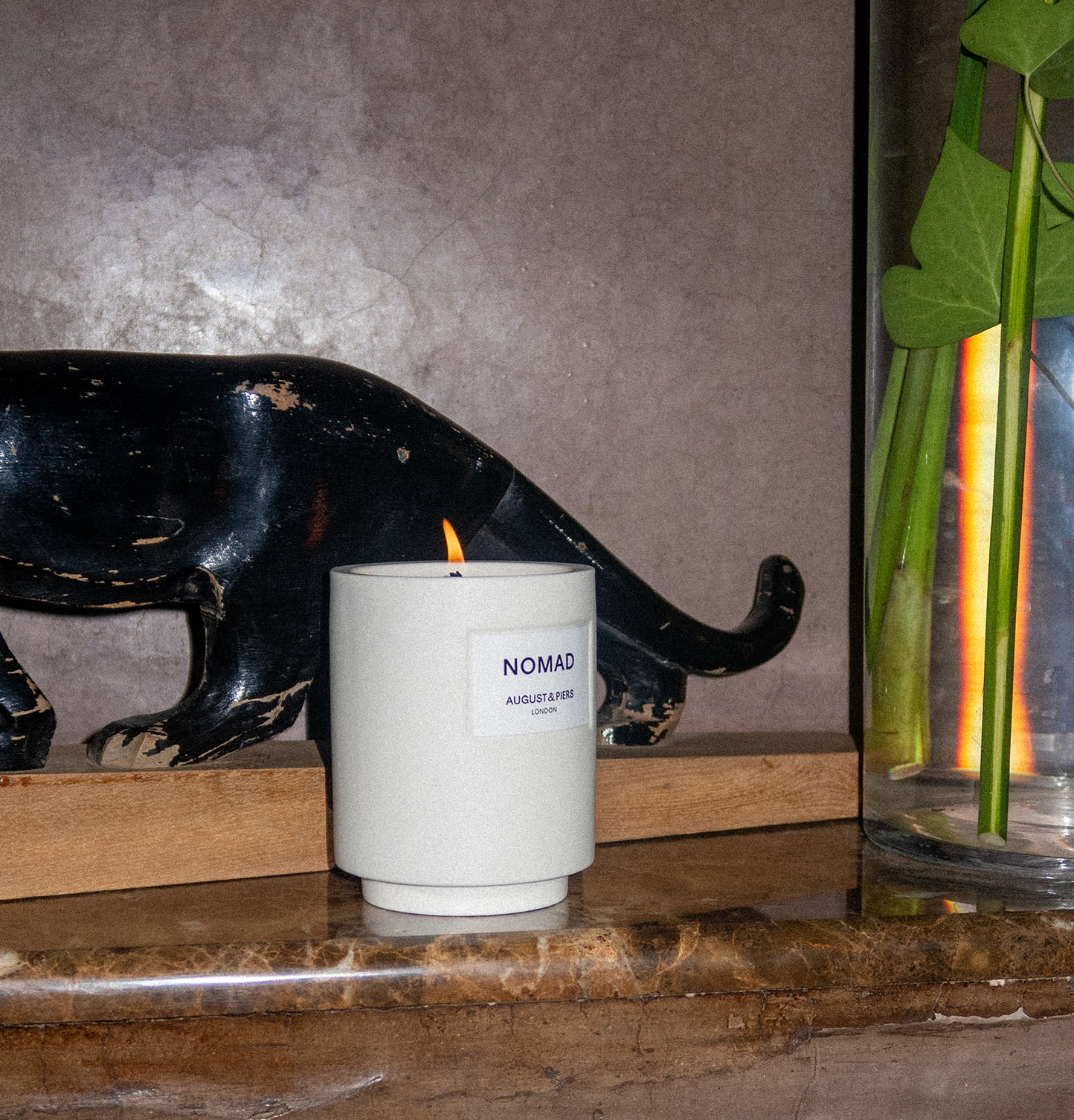 AUGUST&PIERS Nomad luxury scented candle burning on a marble surface, styled with decorative black panther artwork and greenery to create a warm, sophisticated home fragrance setting.
